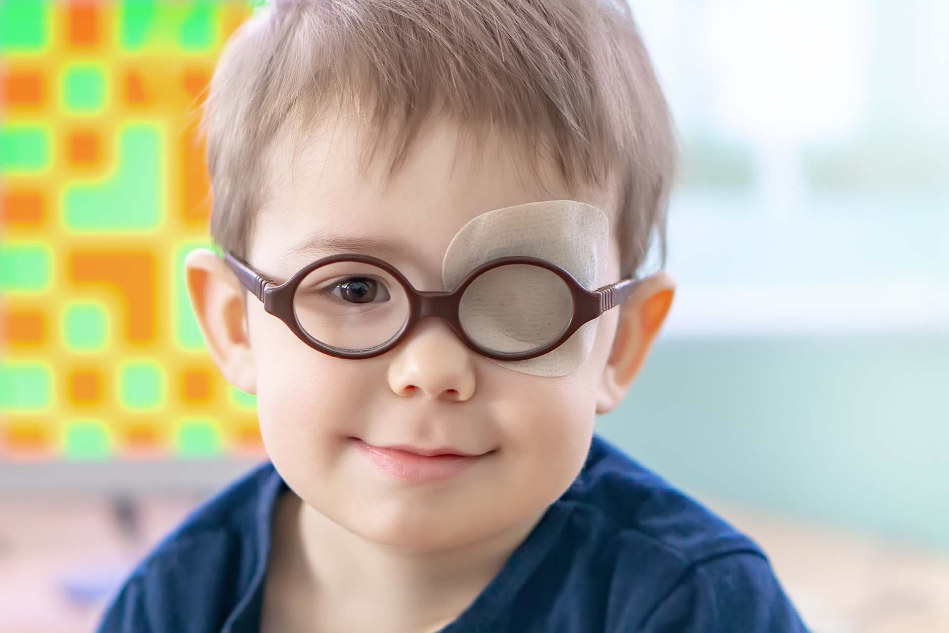 A little boy wearing glasses and an eye patch (plaster, occluder) undergoes a hardware vision treatment to prevent amblyopia and strabismus (squint, lazy eye). Child congenital vision disease problem